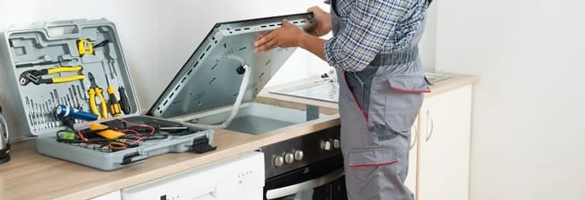 Cooktop repair technician lifting a built-in stovetop for service in Lakewood, CO