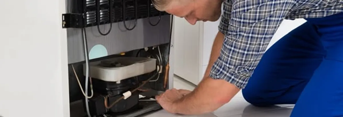 Refrigerator repair technician servicing the compressor and condenser area in Lakewood, CO