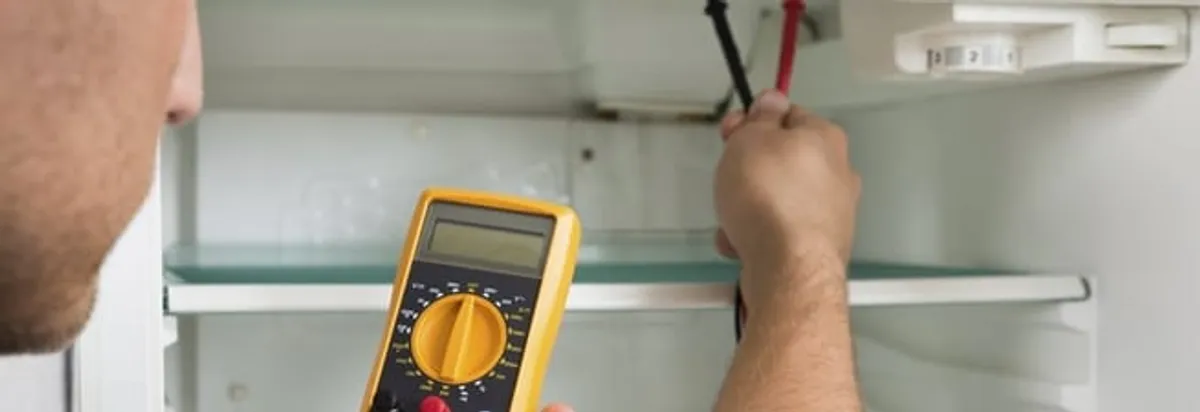 Refrigerator repair technician testing electrical components with a multimeter in Lakewood, CO
